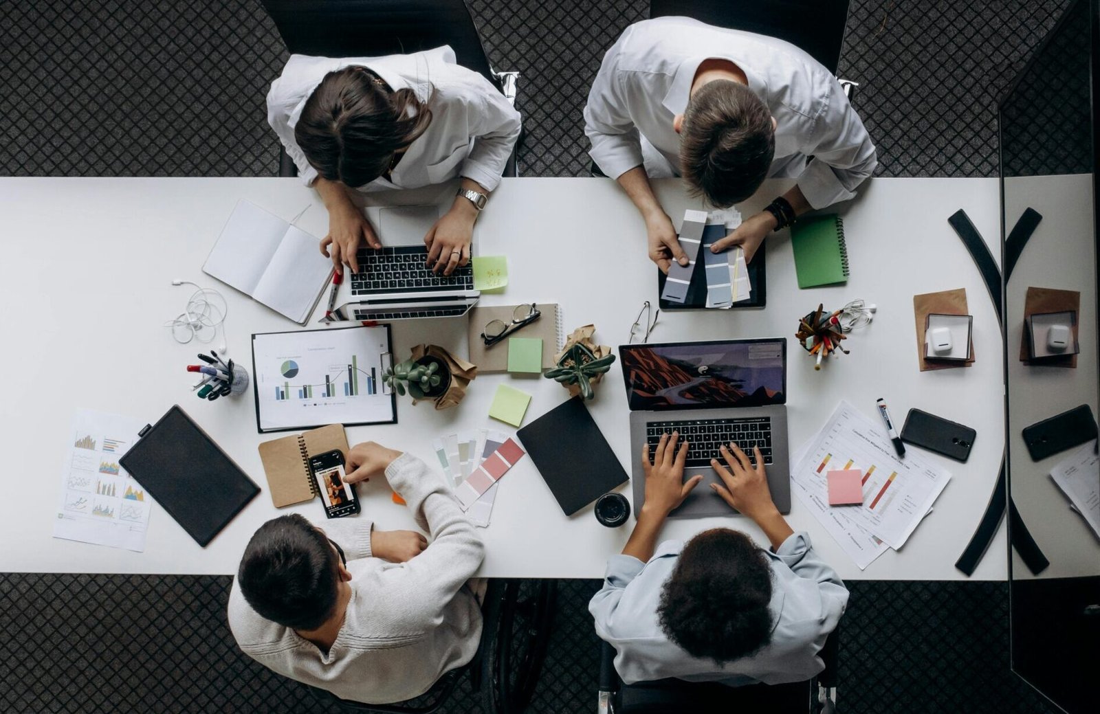 Teamwork in modern office with laptops, charts, and electronic devices from above.