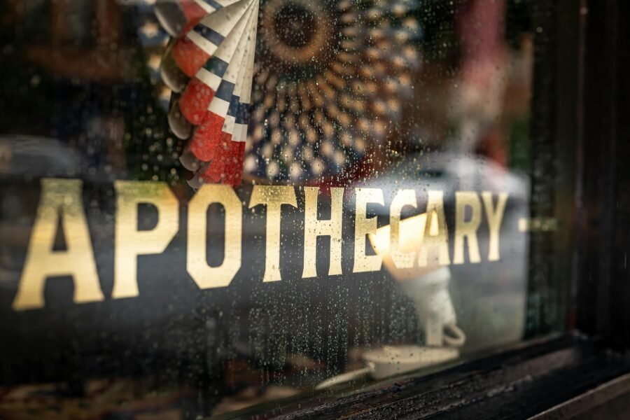 Close-up of a rainy apothecary shop window with decorative signage and reflections.